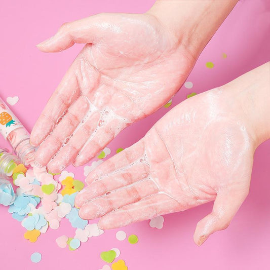 Soapy hands washing with colorful confetti and a bottle on pink background, skincare hygiene